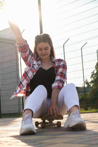 Young millennial woman hippie sitting on skateboard. Summer Skate Sessions. Woman cruising on a longboard in a park. Carefree female skater 20s enjoying freedom youth lifestyle - Zdjęcie, obraz