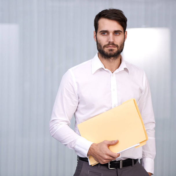 Your information is safe with me. Shot of a handsome young man holding a folder in an office. - Φωτογραφία, εικόνα