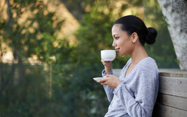 Entspannen Sie mit ihrem Lieblingsgetränk. Aufnahme eines jungen ethnischen Mädchens, das draußen eine Tasse Kaffee genießt. - Foto, Bild