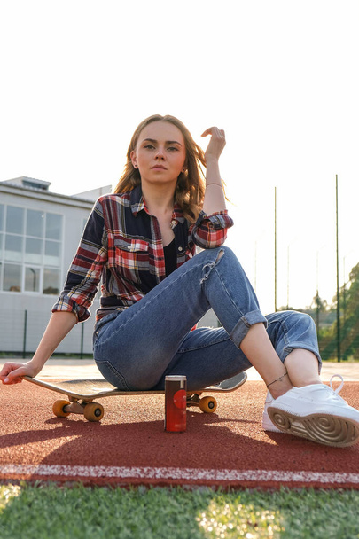 Young millennial woman hippie sitting on skateboard. Summer Skate Sessions. Woman cruising on a longboard in a park. Carefree female skater 20s enjoying freedom youth lifestyle - Photo, Image