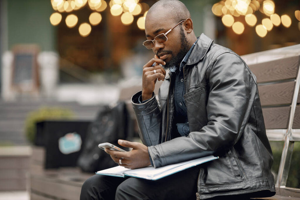 Black man sitting on a bench and using a phone - Fotó, kép
