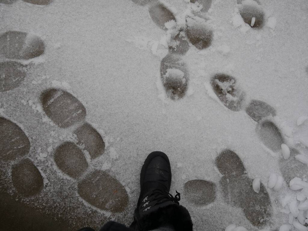 Boot prints in de sneeuw met een grote zwarte laars die op ijs stapt - Foto, afbeelding