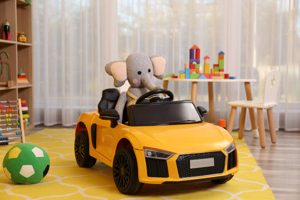 Child's electric car with toy elephant in playroom - Foto, afbeelding