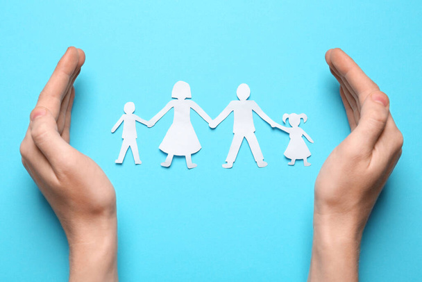 Woman protecting paper cutout of family on light blue background, top view - Foto, imagen