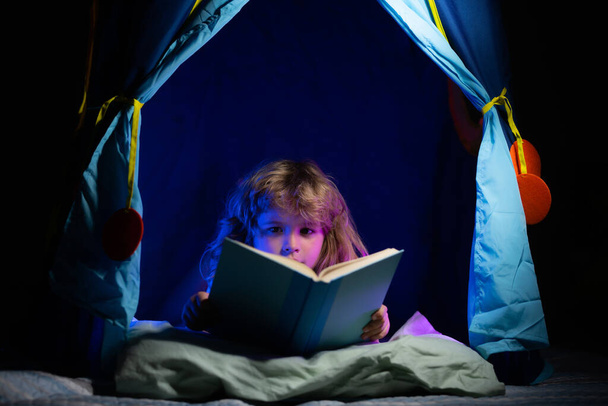 Child in kids tent reading a book in the dark home. Dreaming child read bedtime stories, fairystory or fairytale. - Foto, imagen