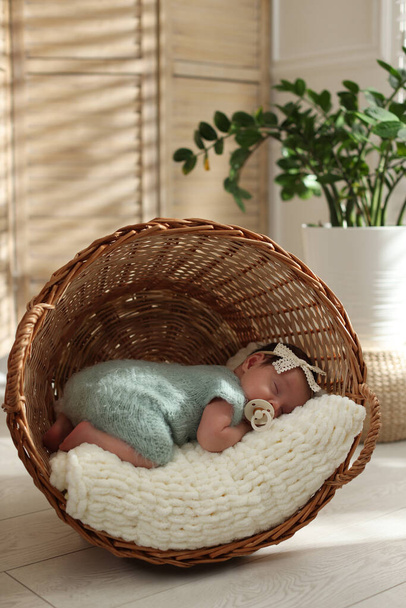 Adorable newborn baby with pacifier sleeping in overturned wicker basket at home - Valokuva, kuva