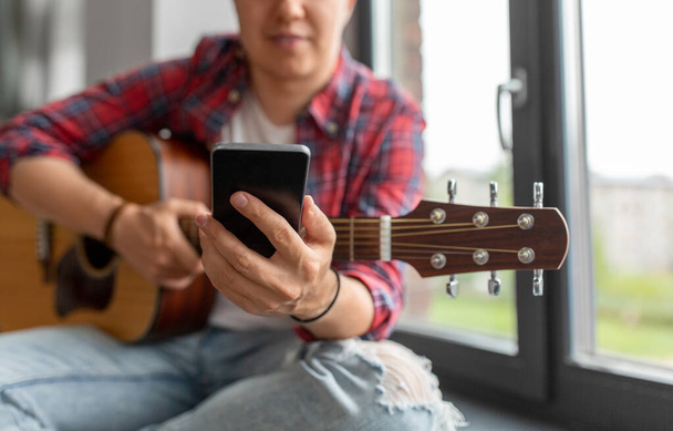 Mann mit Gitarre und Telefon sitzt auf Fensterbank - Foto, Bild
