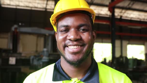 顔のヘッドショットを閉じます:若いエンジニアの肖像画,重工業で働くアフリカ系アメリカ人男性労働者,ヘルメットを身に着けている幸せな専門家,笑顔,カメラを見て幸せな従業員  - 映像、動画