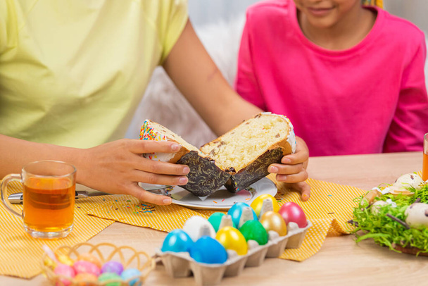 Mom cuts an Easter cake to treat her daughter. African American woman and little girl are sitting at table in festively decorated room at home. Happy easter. Close up. - Foto, Bild
