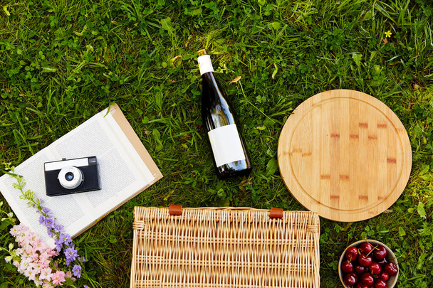 picnic basket, wine, cherry and camera on grass - Photo, Image