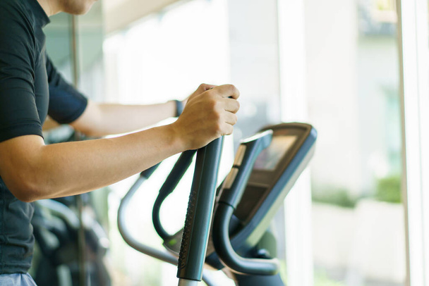 Active Asian young man making a cardio exercise on the elliptical exercise machine in the gym. Fat burn and body muscle building. bodybuilding workout concept. - Photo, image