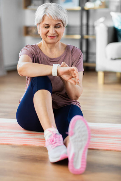 smiling senior woman with fitness tracker at home - Fotó, kép