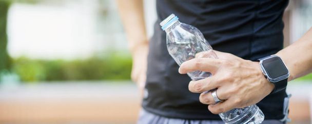 Active Asian sportsman relaxing and drinking a water in bottle after outdoor running or workout. Asian man drink a water during the break from exercise. A healthy man trying hard for cardio workout. - Foto, imagen