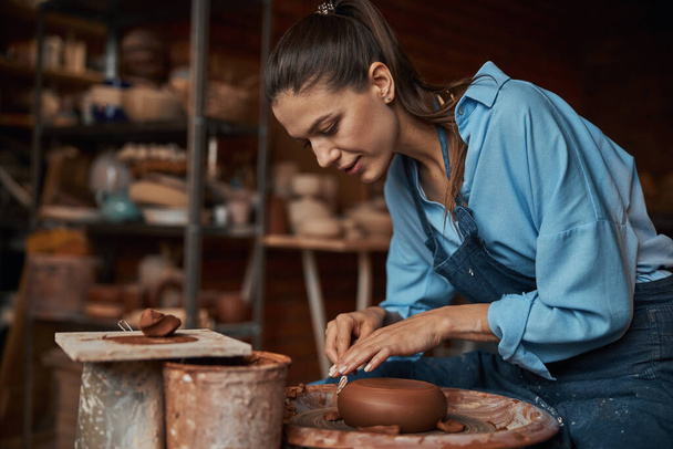 Happy cheerful craft woman shaping earthenware product on special equipments in modern workshop - Фото, зображення