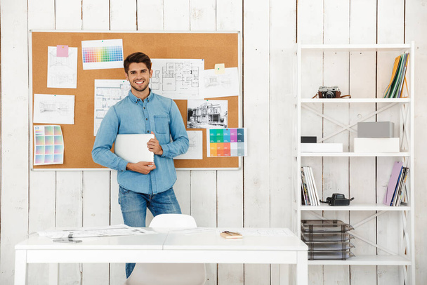 Young white man smiling at camera while standing with laptop in office - Photo, Image