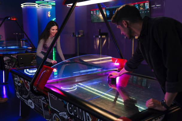 Young man and woman smiling while playing air hockey indoors - Foto, afbeelding