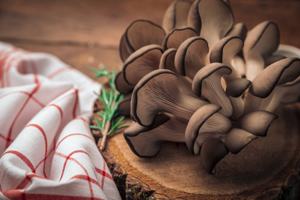 Устричные грибы поверх старинной деревянной доски для рубки и кухонного полотенца, пропагандирующего здоровый образ жизни  - Фото, изображение