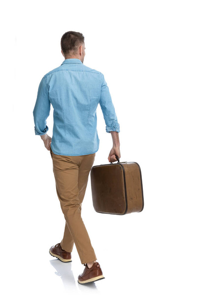 back view of casual guy with baggage going in vacation, travelling around the world, walking away in front of white background - Foto, Imagem