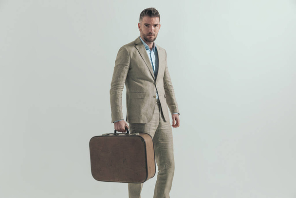 komea liikemies poseeraa puku harmaalla taustalla tilalla matkatavarat ja lähtee kaupungista tärkeä liiketapaaminen  - Valokuva, kuva