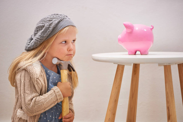 To break or not to break. A cute girl with a hammer eyeing her piggy bank. - Photo, Image