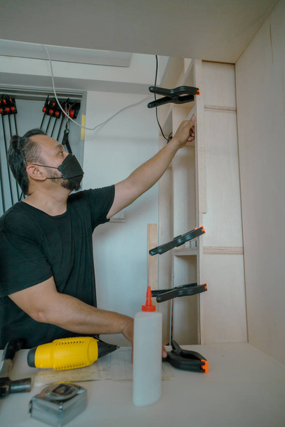 Mann benutzt Klemmen, um Werkstück zu kleben. DIY-Projekt zu Hause. - Foto, Bild