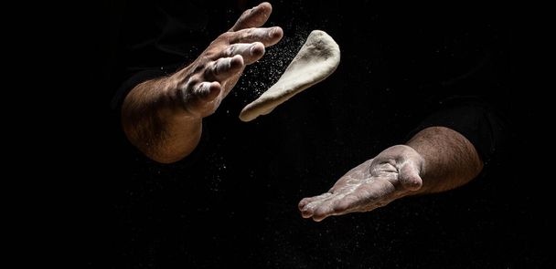 flying pizza dough with flour scattering in a freeze motion of a cloud of flour midair on black. Cook hands kneading dough. copy space. - 写真・画像