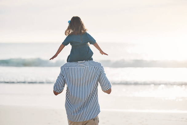 Даддіс маленька дівчинка. Задній погляд на невідомого батька, який носить свою молоду доньку на плечах під час приємного дня на пляжі
. - Фото, зображення