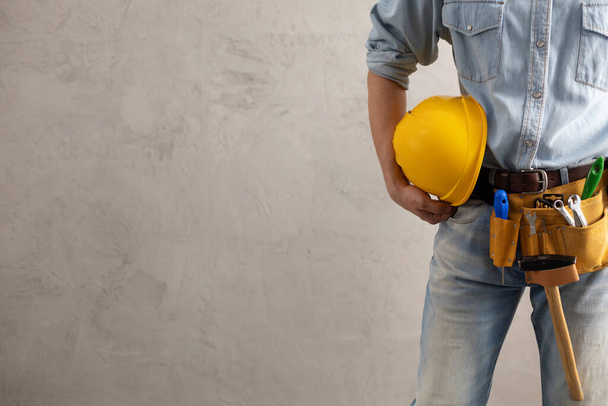 Worker man holding construction helmet tool near concrete or cement wall. Male hand and hard hat for house room renovation. Home renovation concept - Valokuva, kuva