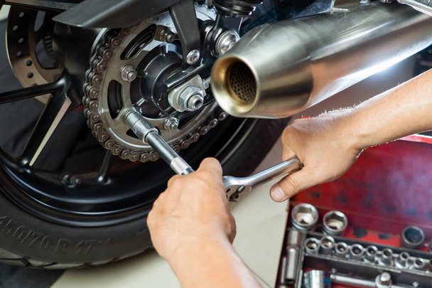 オートバイのスプロケットのレンチそしてソケットを使用して機械的。オートバイのガレージの維持そして修理の概念。  - 写真・画像