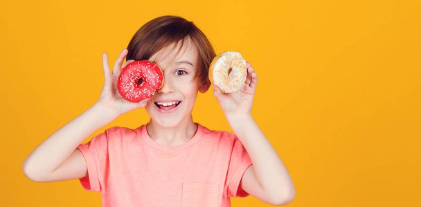 Birthday party. Tasty food for kids. Colored donuts. Fashion, people, lifestyle. Happy child played with donuts on yellow background wall. Kid enjoying sweets. Cute funny boy holding donuts eyes. - Photo, Image
