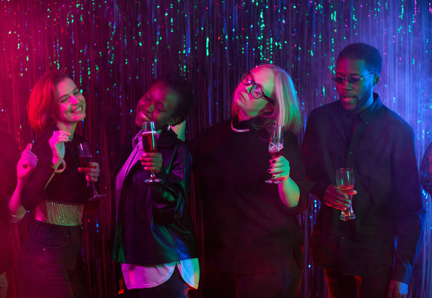 Diverse group of people vibing at party and holding drinks in neon light - Zdjęcie, obraz