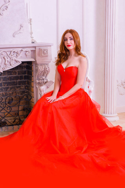 Wspaniała młoda kobieta w luksusowej czerwonej sukience i cennej biżuterii pozowanie w luksusowym apartamencie. Klasyczne klasyczne wnętrze. Piękno luksusowe mody - Zdjęcie, obraz