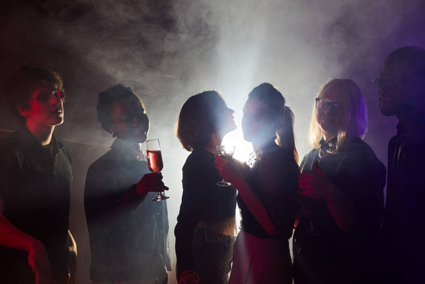 Podświetlany ujęcie młodych ludzi tańczących na imprezie, sylwetki w klubie dymnym - Zdjęcie, obraz