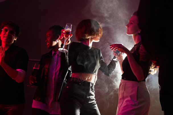 Podświetlany portret dwóch młodych kobiet tańczących w tłumie podczas zabawy w klubie dymnym, przestrzeń do kopiowania - Zdjęcie, obraz