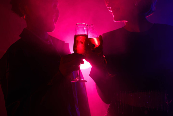 Taustavalaistu muotokuva kahdesta nuoresta naisesta nauttimassa juomasta samalla kun juhlitaan savuisessa klubissa neonvalojen kanssa, kopioi tilaa - Valokuva, kuva