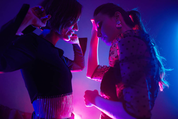 Przycięte ujęcie dwóch młodych kobiet tańczących razem w klubie oświetlonym różowymi neonami - Zdjęcie, obraz