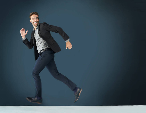 Running after his goals. Shot of a young businessman running against a dark background. - Foto, imagen