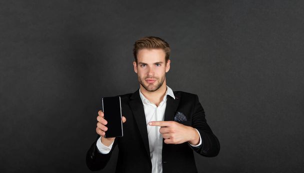Professional manager in suit pointing finger at mobile device dark background copy space, phone - Фото, изображение