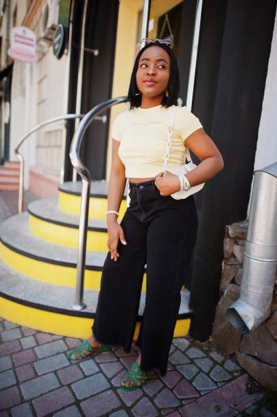 Beautiful fashionable young african american woman posing in street stairs, sunglasses, yellow top. Fashion summer photo. Bright colors. Nice view afro people. - Foto, Imagen