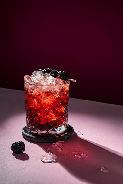 Summer cold cocktail drink with ice garnished with blackberry on dramatic violet background - Photo, Image