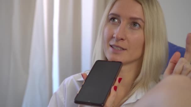 eine Frau zu Hause nimmt eine Sprachnachricht auf ihrem Smartphone auf, während sie im Bett liegt. - Filmmaterial, Video