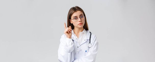 Медичні працівники, медицина, страхування та концепція пандемії ковадла-19 . Розумна професійна жінка-лікарка в білих скрабах і окулярах, мають ідею, пропозицію, піднімають індексний знак пальця еврика
 - Фото, зображення