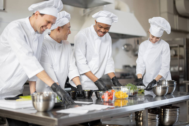 Multiraciální tým kuchařů míchání ingrediencí pro odnést jídlo v profesionální kuchyni - Fotografie, Obrázek