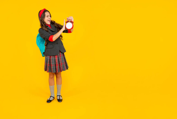 unhappy child in school uniform with backpack with loud alarm clock on copy space, time. - Φωτογραφία, εικόνα