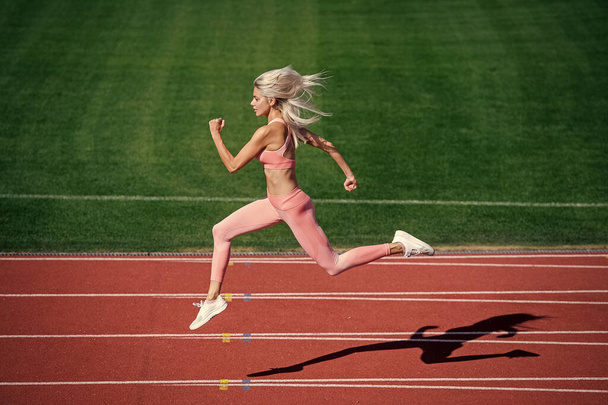 fit lady in fitness wear running on stadium racetrack while sport workout, energy - Photo, image