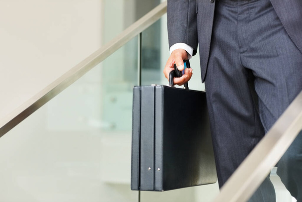 Liikemies, joka kantaa kännykkää ja matkalaukkua. Matala osuus liikemies kuljettaa matkapuhelin ja matkalaukku ja kävely alas portaita. - Valokuva, kuva