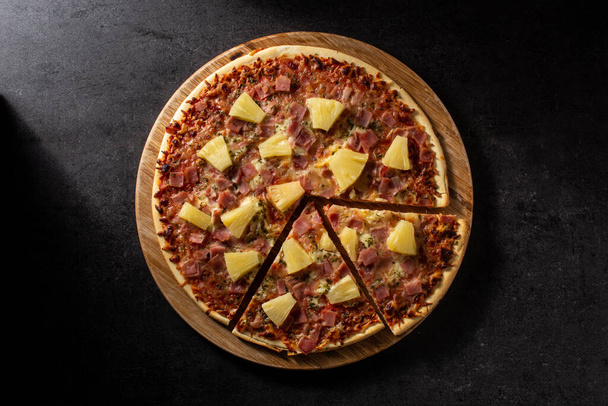 Pizza hawaiana con piña, jamón y queso sobre fondo de pizarra negra - Foto, imagen