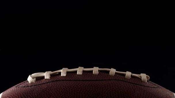 American Football und Sport Night Veranstaltungskonzept mit Nahaufnahme an den Schnürsenkeln eines Lederballs isoliert auf schwarzem Hintergrund mit dramatischem Licht von einer Seite beleuchtet und Kopierfläche für Text - Foto, Bild