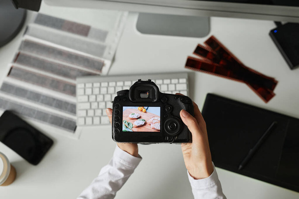 Vista superior de primer plano de la fotógrafa sosteniendo la cámara con la imagen en la pantalla mientras edita fotos en el lugar de trabajo - Foto, Imagen