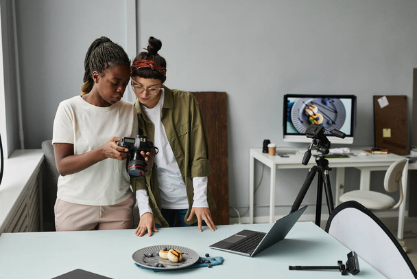 写真スタジオ、コピースペースで作業中にカメラで写真を見ている2人の女性写真家の肖像 - 写真・画像